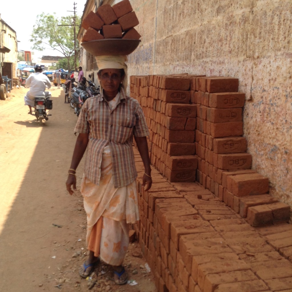 Building site worker carrying 8 bricks on her head back and forth all day in the scorching sun and ferocious heat.